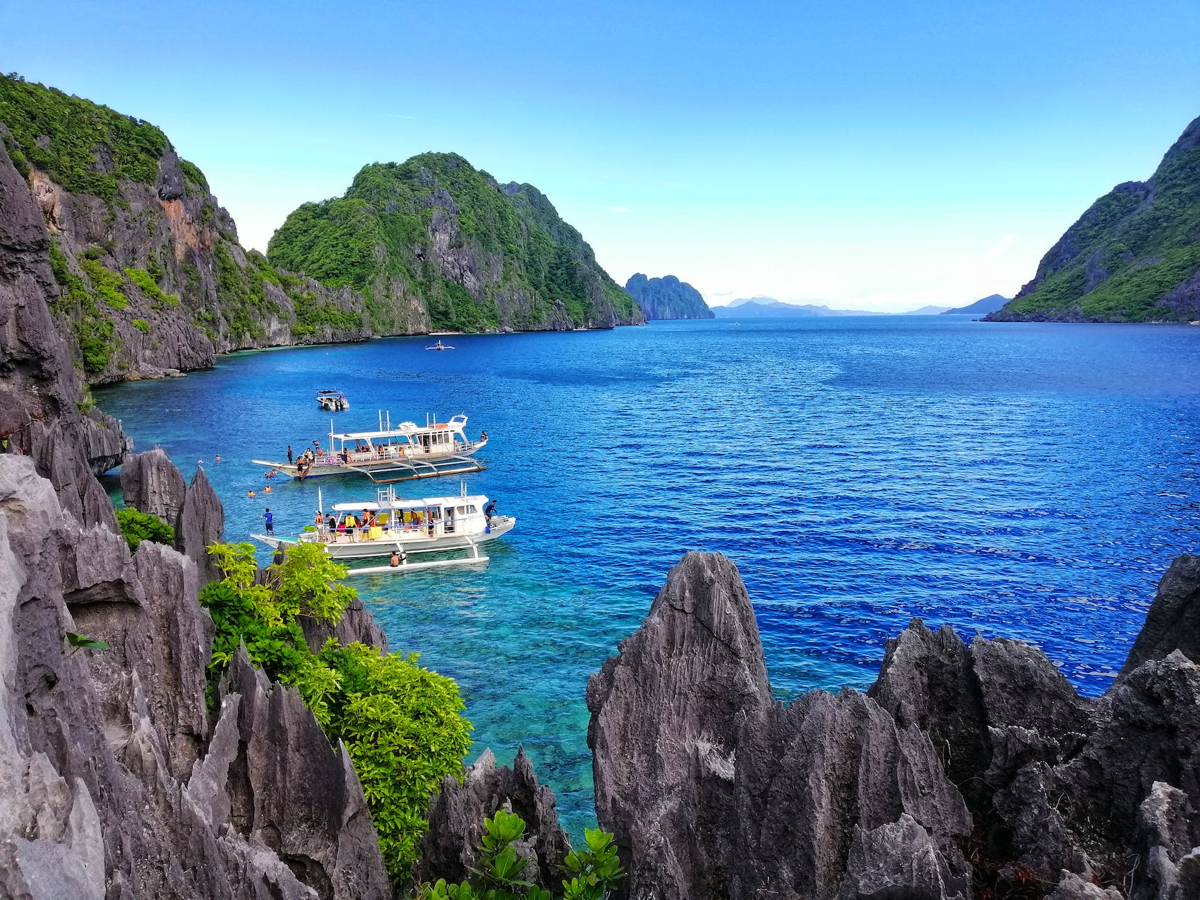 white boats on sea near the gray rock formation